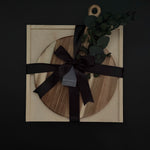 Wooden circular cutting board with black ribbon and decorative leaves on a dark background