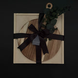 Wooden circular cutting board with black ribbon and decorative leaves on a dark background