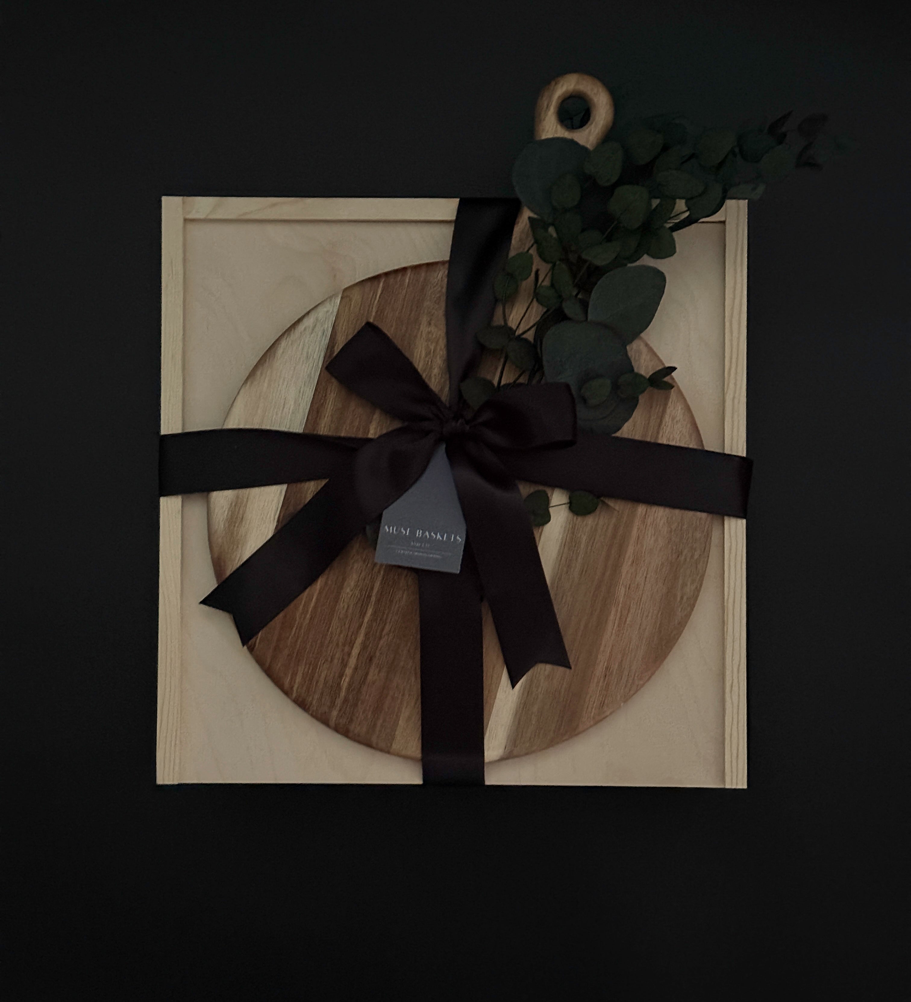 Wooden circular cutting board with black ribbon and decorative leaves on a dark background