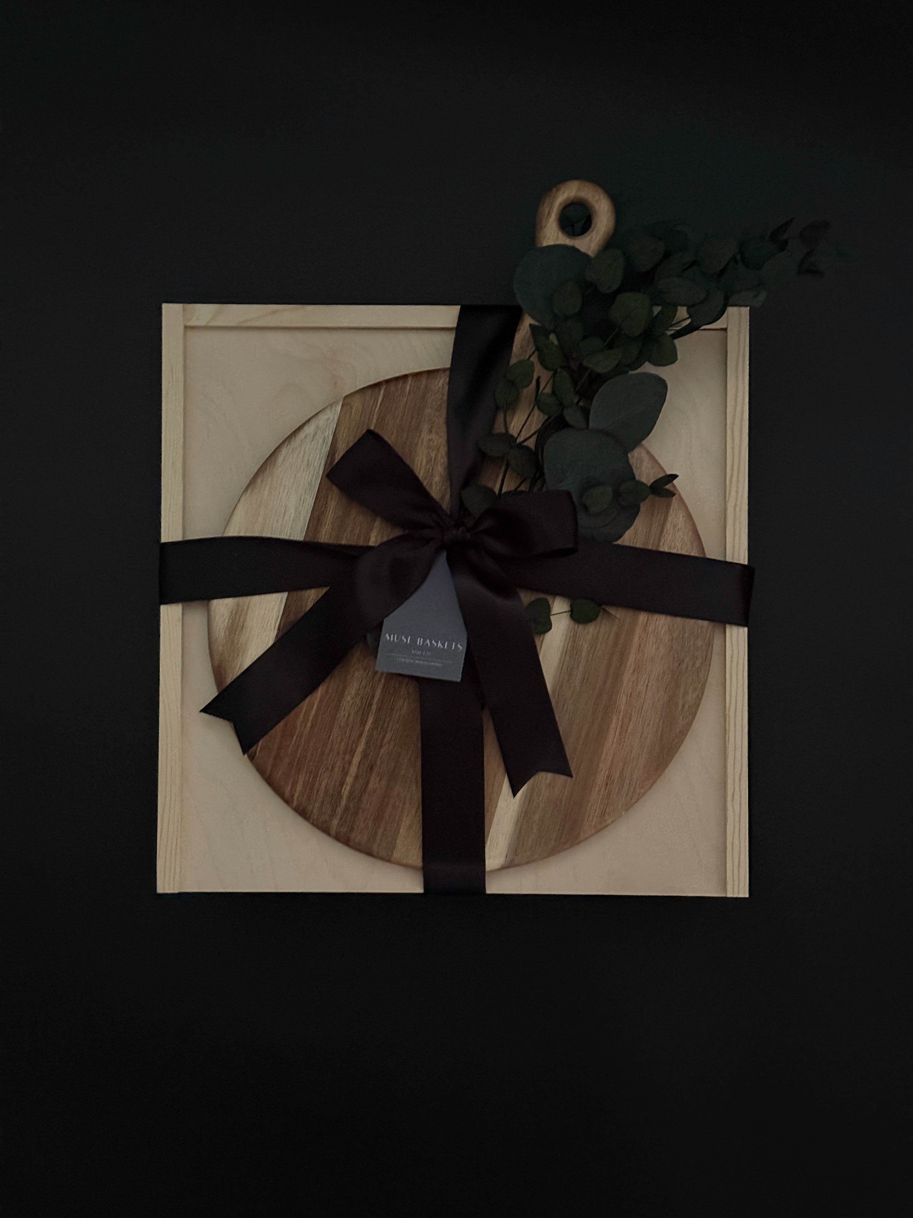 Wooden circular cutting board with black ribbon and decorative leaves on a dark background