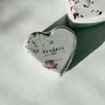Close-up of a Reverie heart-shaped bath bomb with dried floral accents, a self-care product featured in Muse Baskets and Co. gift baskets
