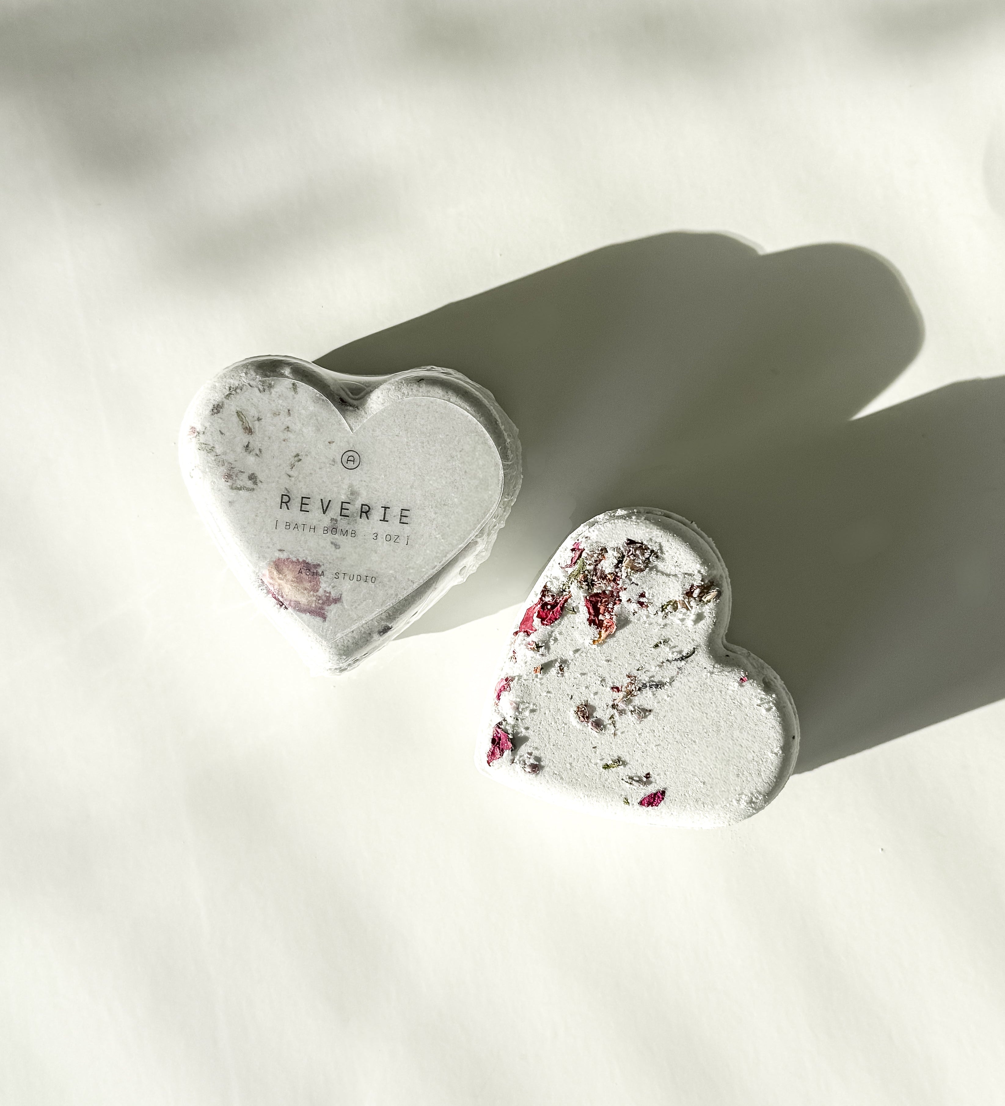 Two Reverie heart-shaped bath bombs with dried floral accents, a self-care product featured in Muse Baskets and Co. gift baskets