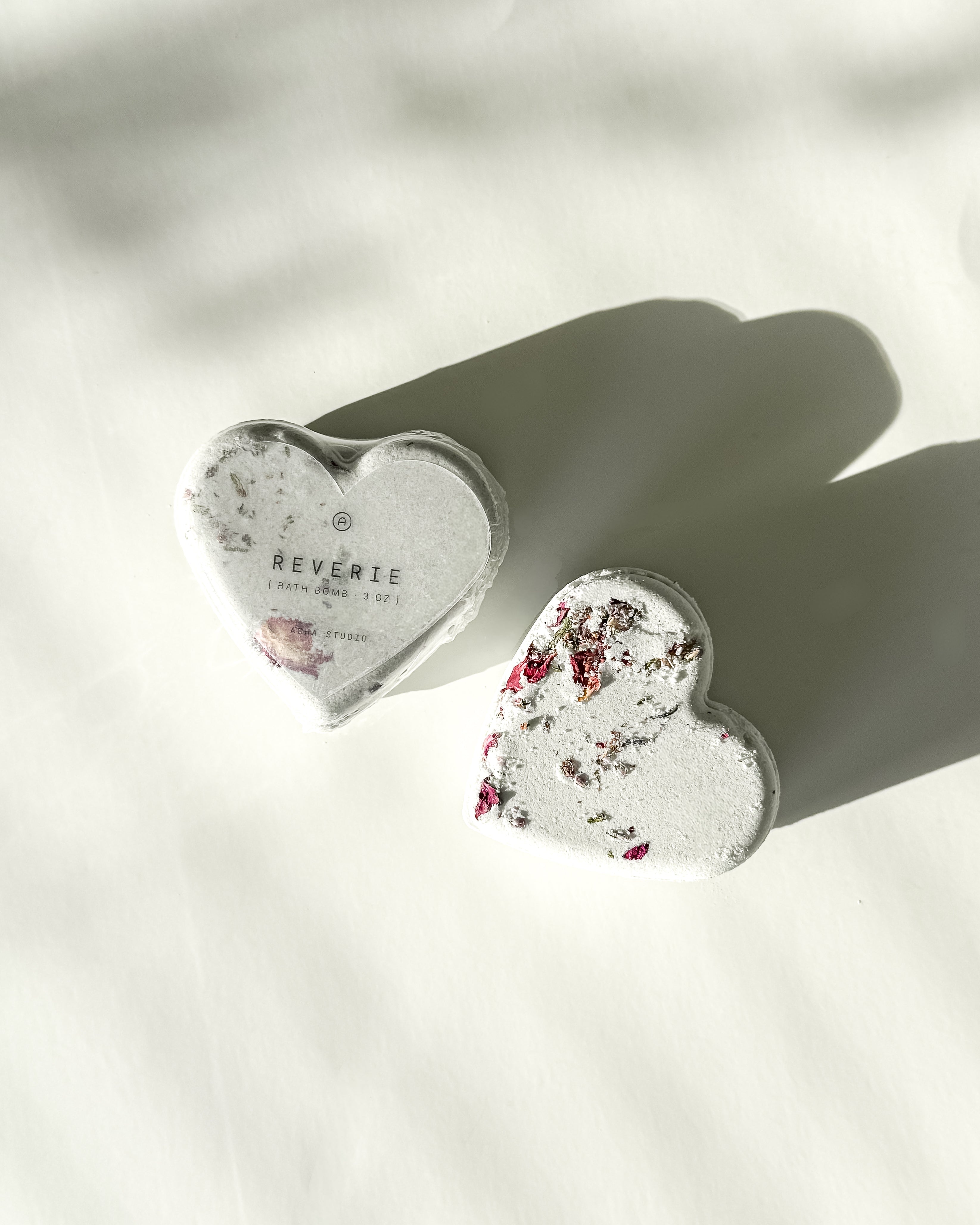 Two Reverie heart-shaped bath bombs with dried floral accents, a self-care product featured in Muse Baskets and Co. gift baskets
