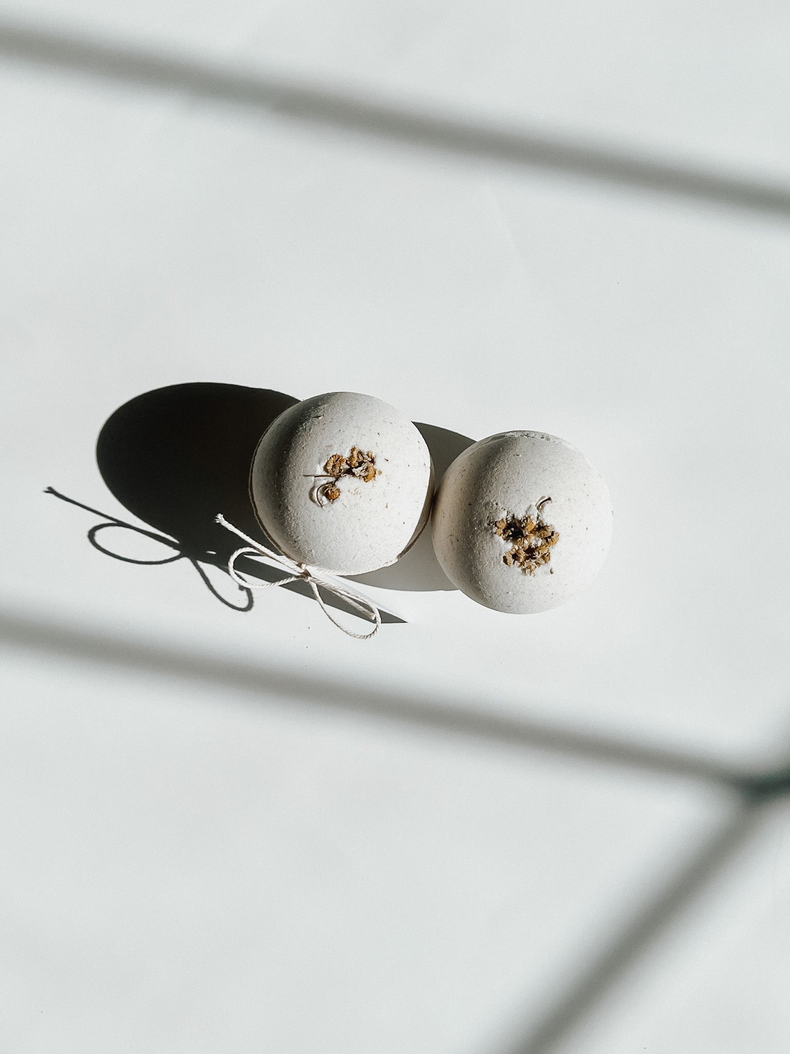 Two round bath bombs decorated with dried flowers and tied with twine, a self-care product featured in Muse Baskets and Co. gift baskets
