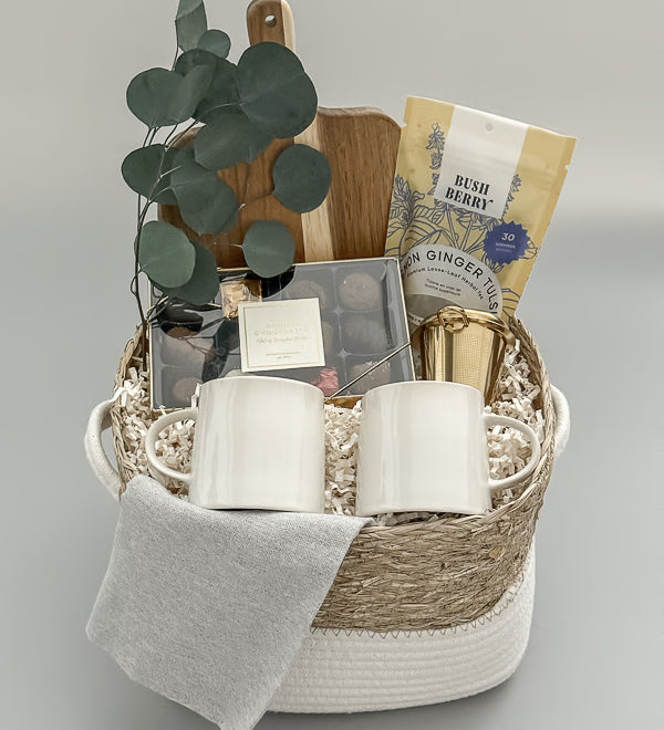 Luxury tea and chocolate gift basket with gold tea steeper, stoneware mugs, and Canadian artisanal treats, presented in a woven basket with satin ribbon