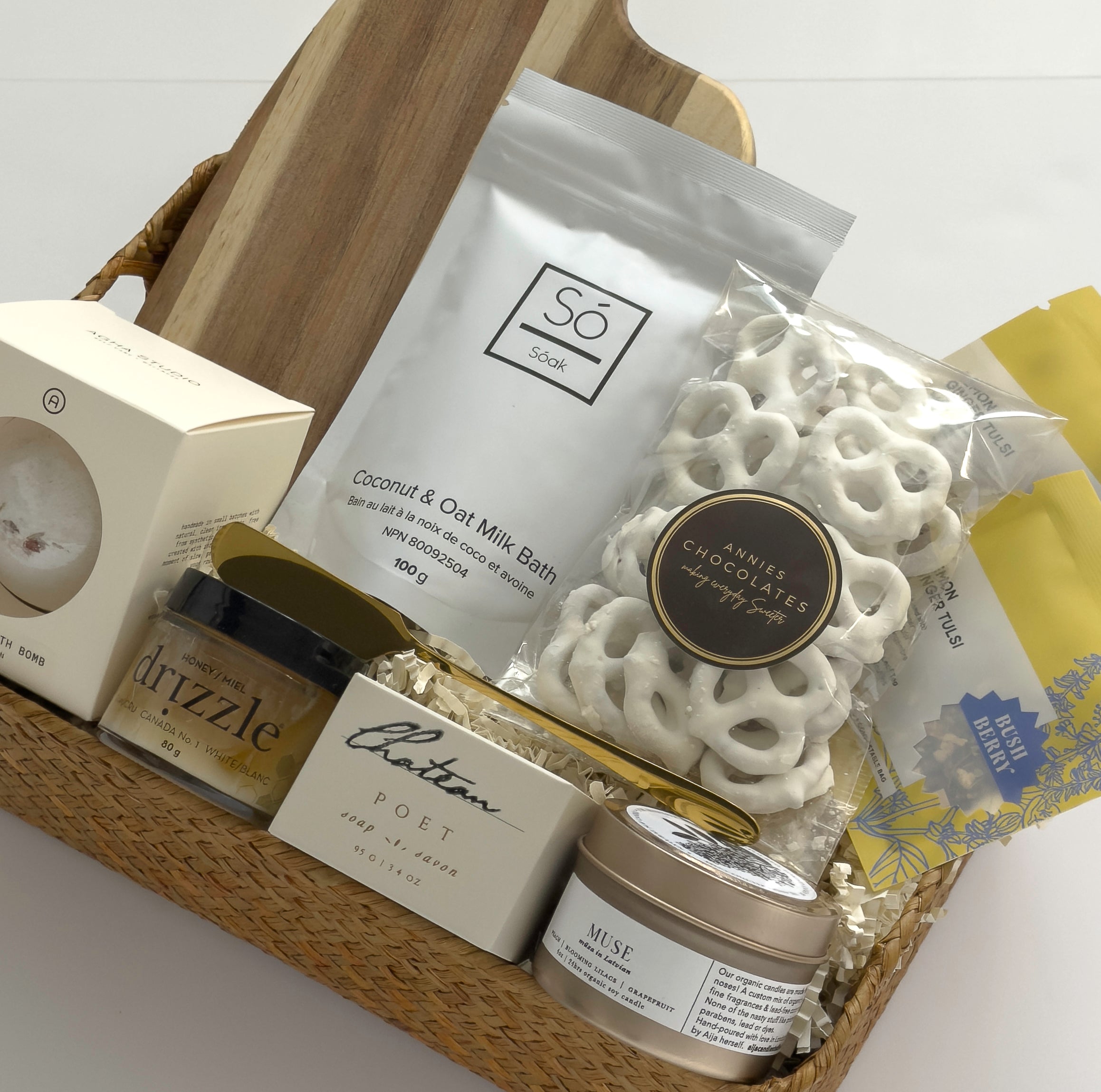 Canadian gift basket by Muse Baskets and Co. with acacia board, Drizzle honey, Bush Berry tea, Muse candle, chocolate pretzels and bath essentials.