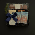 The Chocolate Indulgence gift box with artisan chocolate bar, hot chocolate mixes, sandwich cookies, and holiday accents in a black gift box.