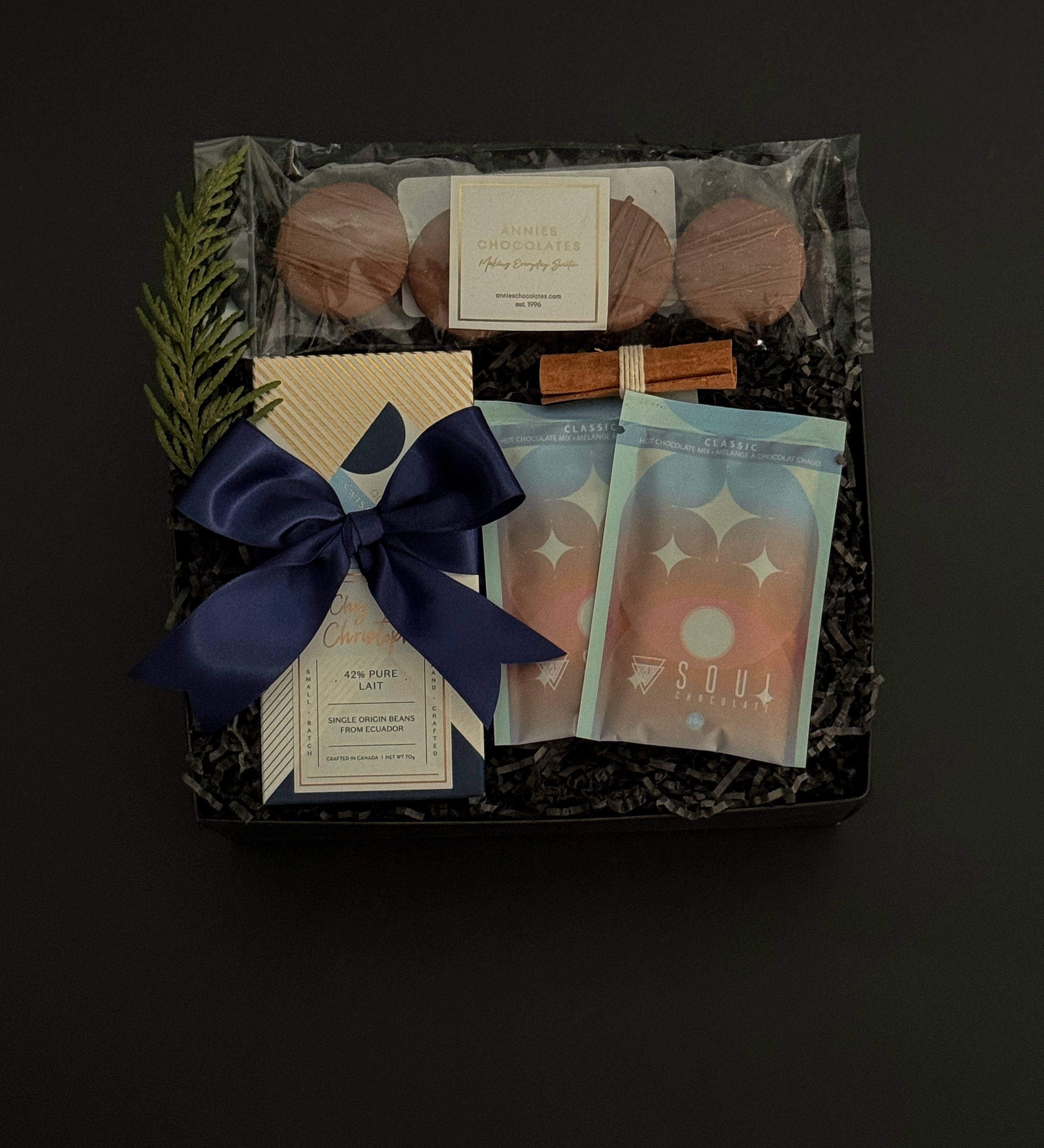 The Chocolate Indulgence gift box with artisan chocolate bar, hot chocolate mixes, sandwich cookies, and holiday accents in a black gift box.