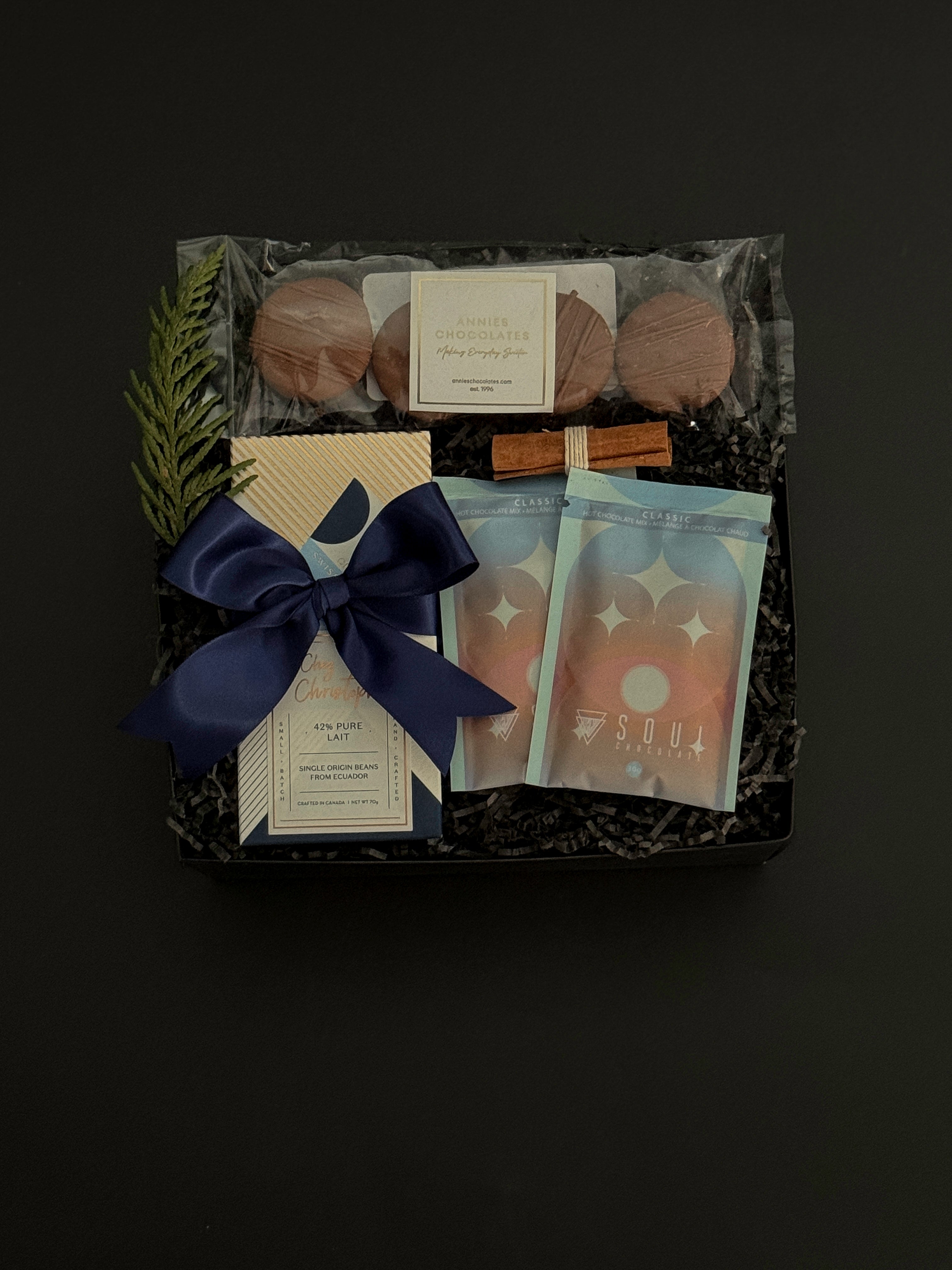 The Chocolate Indulgence gift box with artisan chocolate bar, hot chocolate mixes, sandwich cookies, and holiday accents in a black gift box.