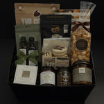 The Gathered Home gift basket by Muse Baskets and Co. photographed straight on, with YVR Cookie crisps, Roger's espresso beans, Annie's chocolate popcorn, Bliss buttercream cookies, All of Oils olive oil and balsamic, Provisions wine jam, SaltSpring candied jalapeño relish, a Jocelyn & Co. dipping dish, and a Laurel Leaf and Olive candle by Noel & Co. in a black box, a curated client and corporate housewarming gift from Canadian makers.