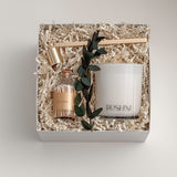 Lumière gift box by Muse Baskets and Co. shown from above, featuring a white Roshni candle, a gold candle snuffer, white tipped home matches in a glass jar, and a preserved eucalyptus stem arranged on natural fill in a white box, a refined realtor closing gift, possession day gift, and corporate gift.