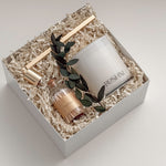 Lumière gift box by Muse Baskets and Co. photographed at an angle, with a white Roshni candle, gold candle snuffer, white tipped home matches, and preserved eucalyptus nestled in a white gift box, a calming sympathy gift, client care gift, and homeowner welcome gift from Canadian makers.
