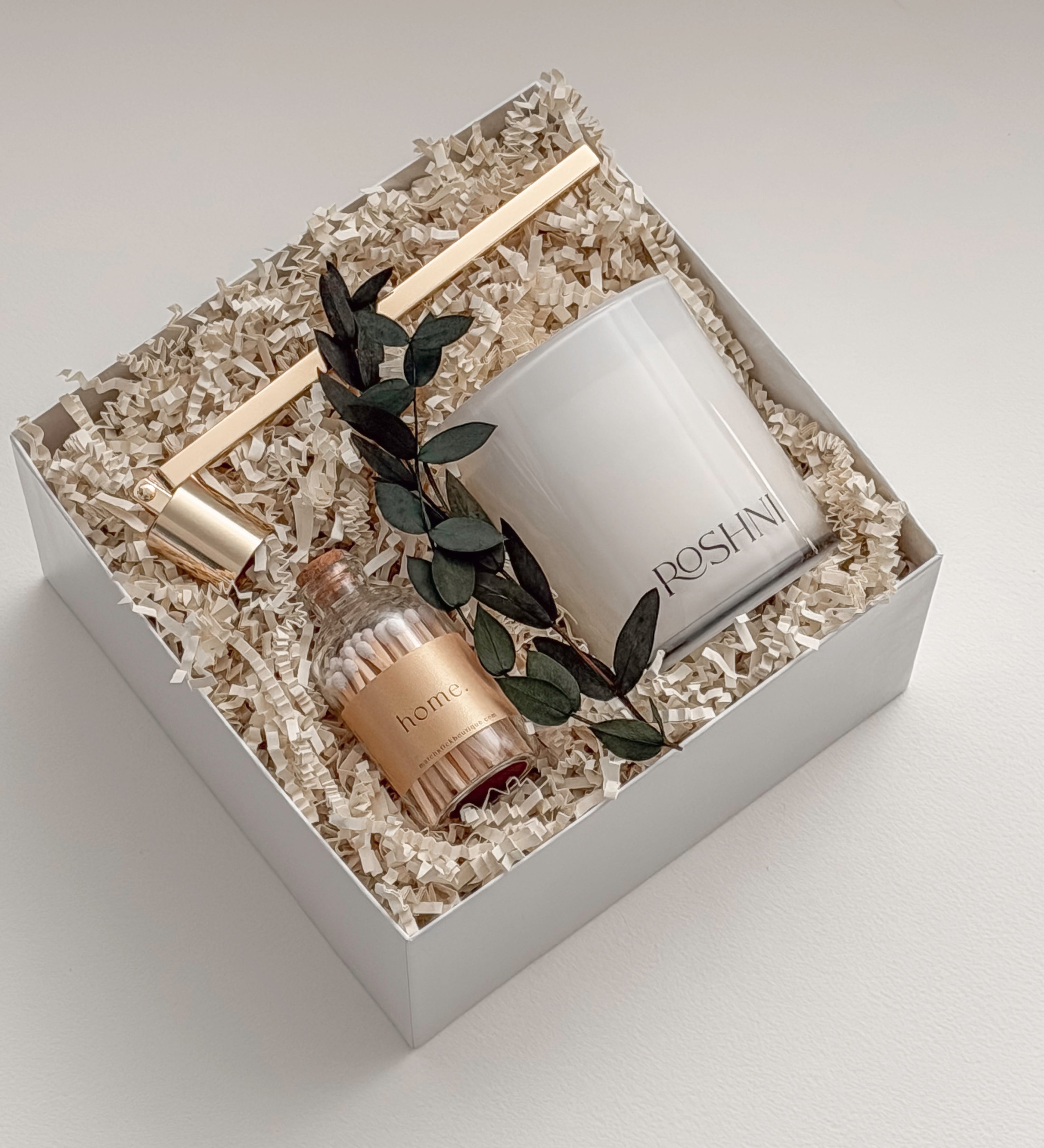 Lumière gift box by Muse Baskets and Co. photographed at an angle, with a white Roshni candle, gold candle snuffer, white tipped home matches, and preserved eucalyptus nestled in a white gift box, a calming sympathy gift, client care gift, and homeowner welcome gift from Canadian makers.
