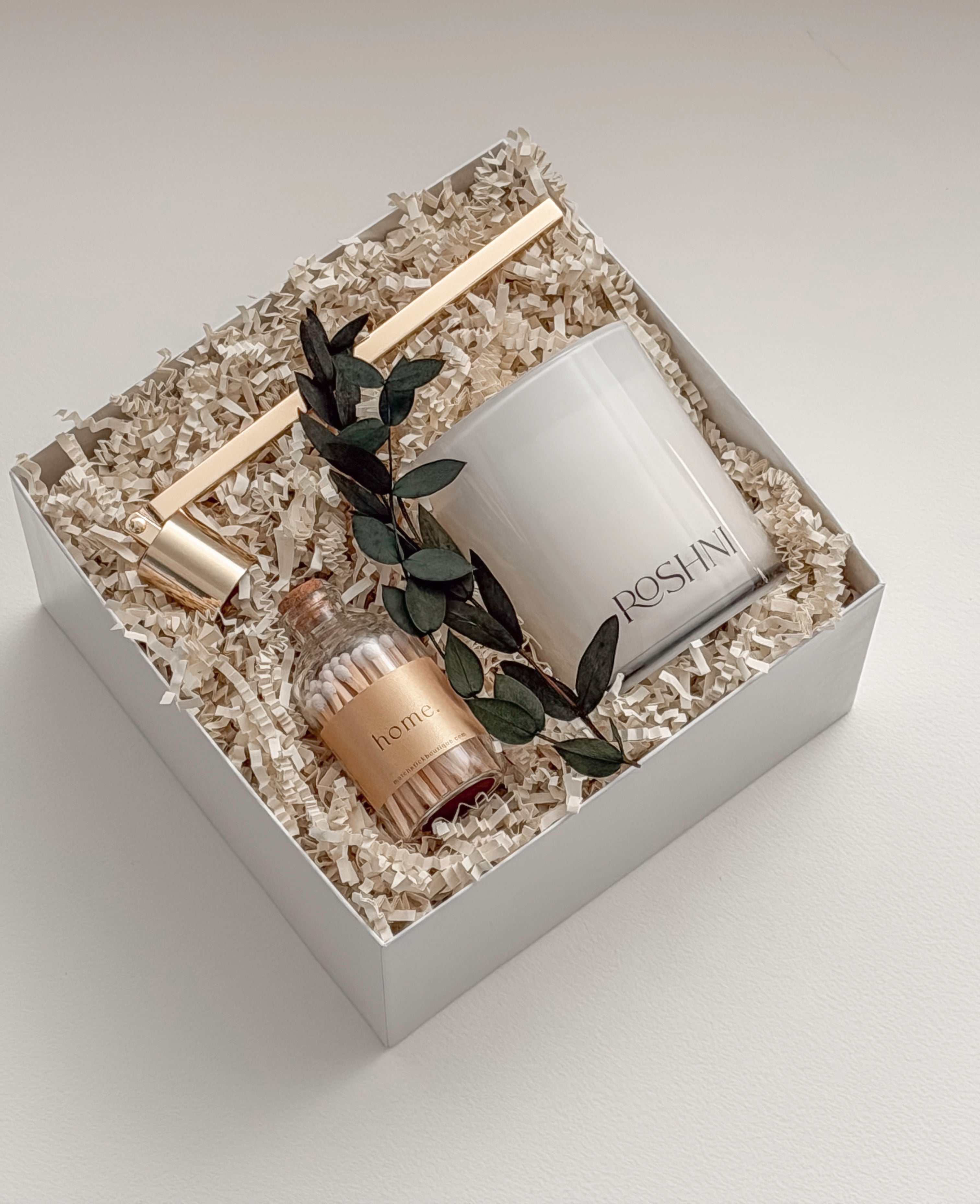 Lumière gift box by Muse Baskets and Co. photographed at an angle, with a white Roshni candle, gold candle snuffer, white tipped home matches, and preserved eucalyptus nestled in a white gift box, a calming sympathy gift, client care gift, and homeowner welcome gift from Canadian makers.