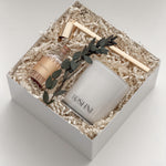 Lumière gift box by Muse Baskets and Co. viewed from the side, showing a white Roshni candle, gold candle snuffer, glass jar of white tipped home matches, and preserved eucalyptus on natural fill in a white box, a curated possession day gift, realtor closing gift, and corporate gift with Canada-wide delivery.
