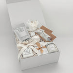 Gift box with various items including a candle, soap, and a small plant on a light gray background