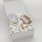 Gift box with various items including a candle, soap, and a small plant on a light gray background