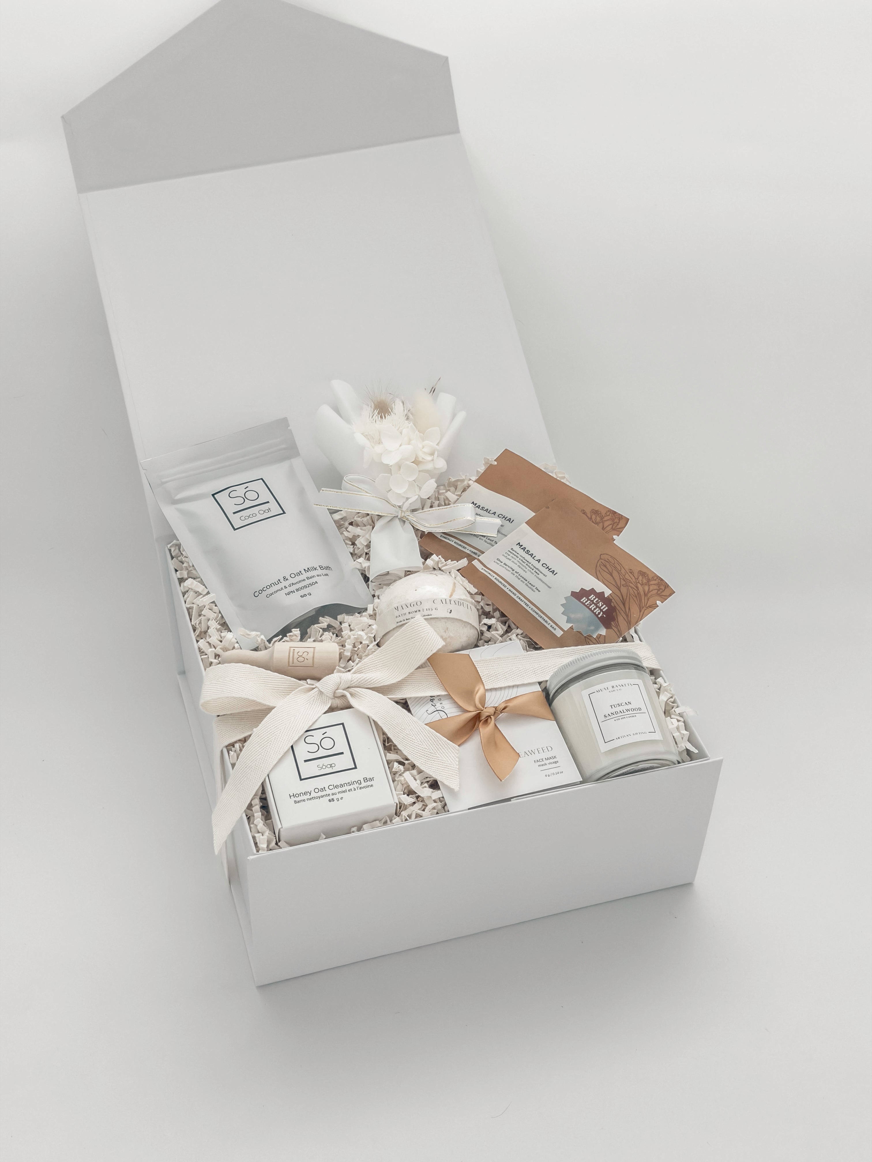 Gift box with various items including a candle, soap, and a small plant on a light gray background