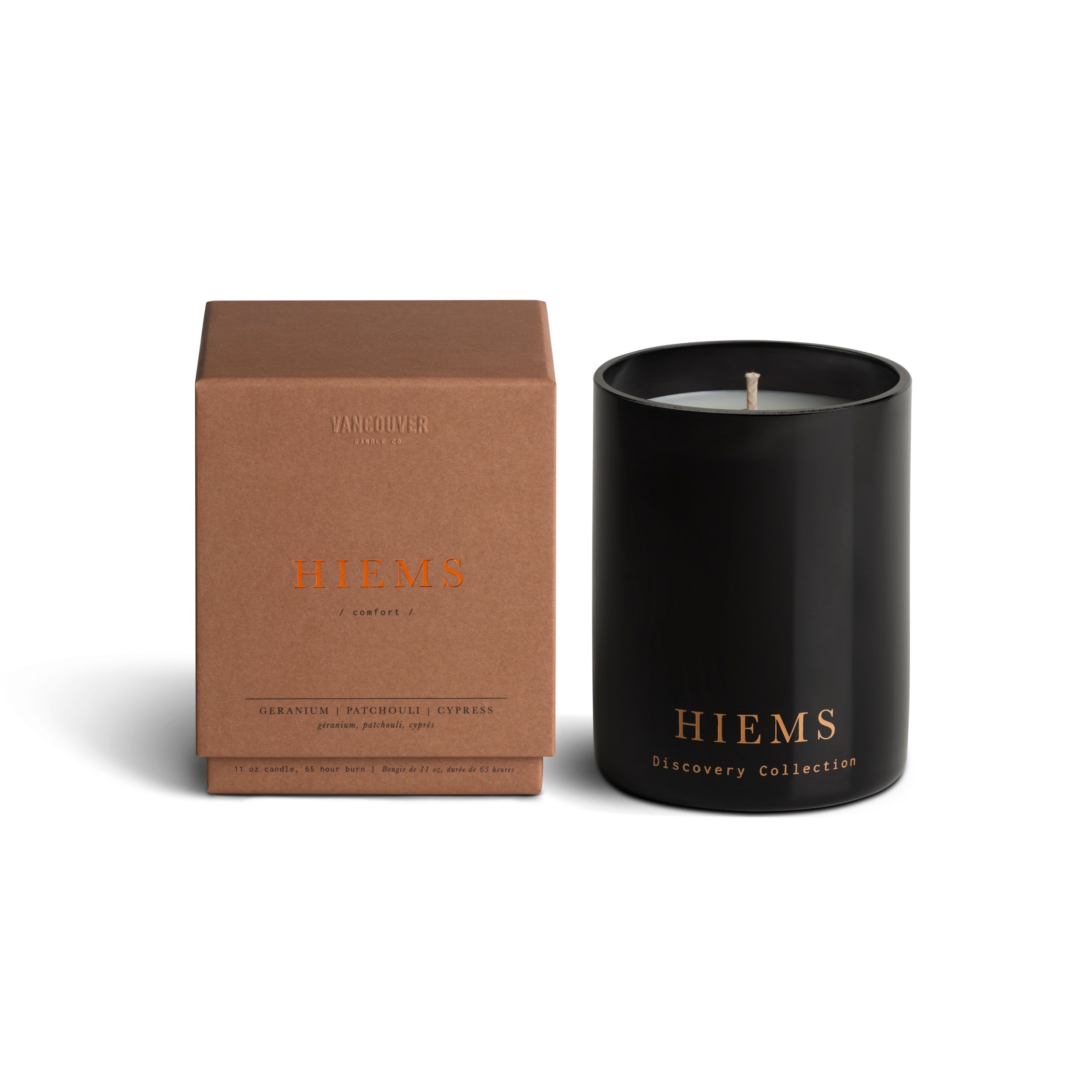 Vancouver Candle Co. Hiems candle in geranium, patchouli, and cypress, shown beside its packaging, a premium candle featured in Muse Baskets and Co. corporate gift baskets