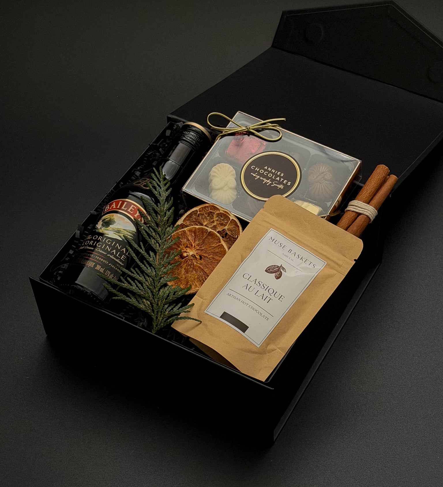 Holiday gift box by Muse Baskets and Co. featuring Baileys, Canadian chocolates, hot chocolate and cinnamon in a signature onyx presentation box.