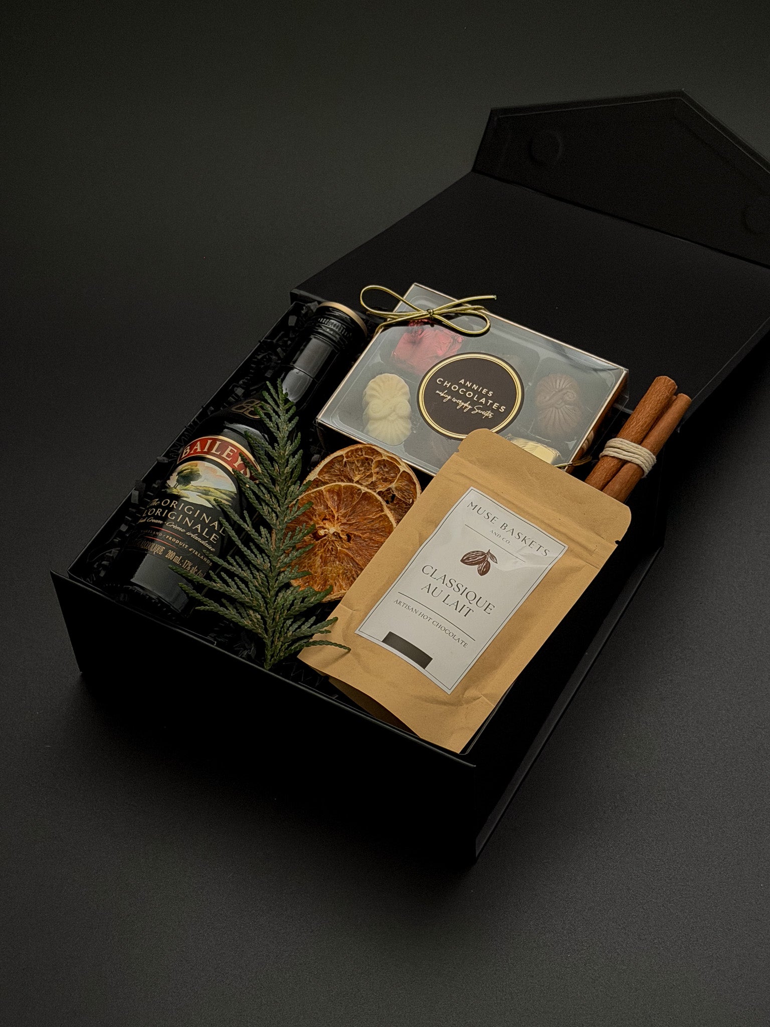 Holiday gift box by Muse Baskets and Co. featuring Baileys, Canadian chocolates, hot chocolate and cinnamon in a signature onyx presentation box.