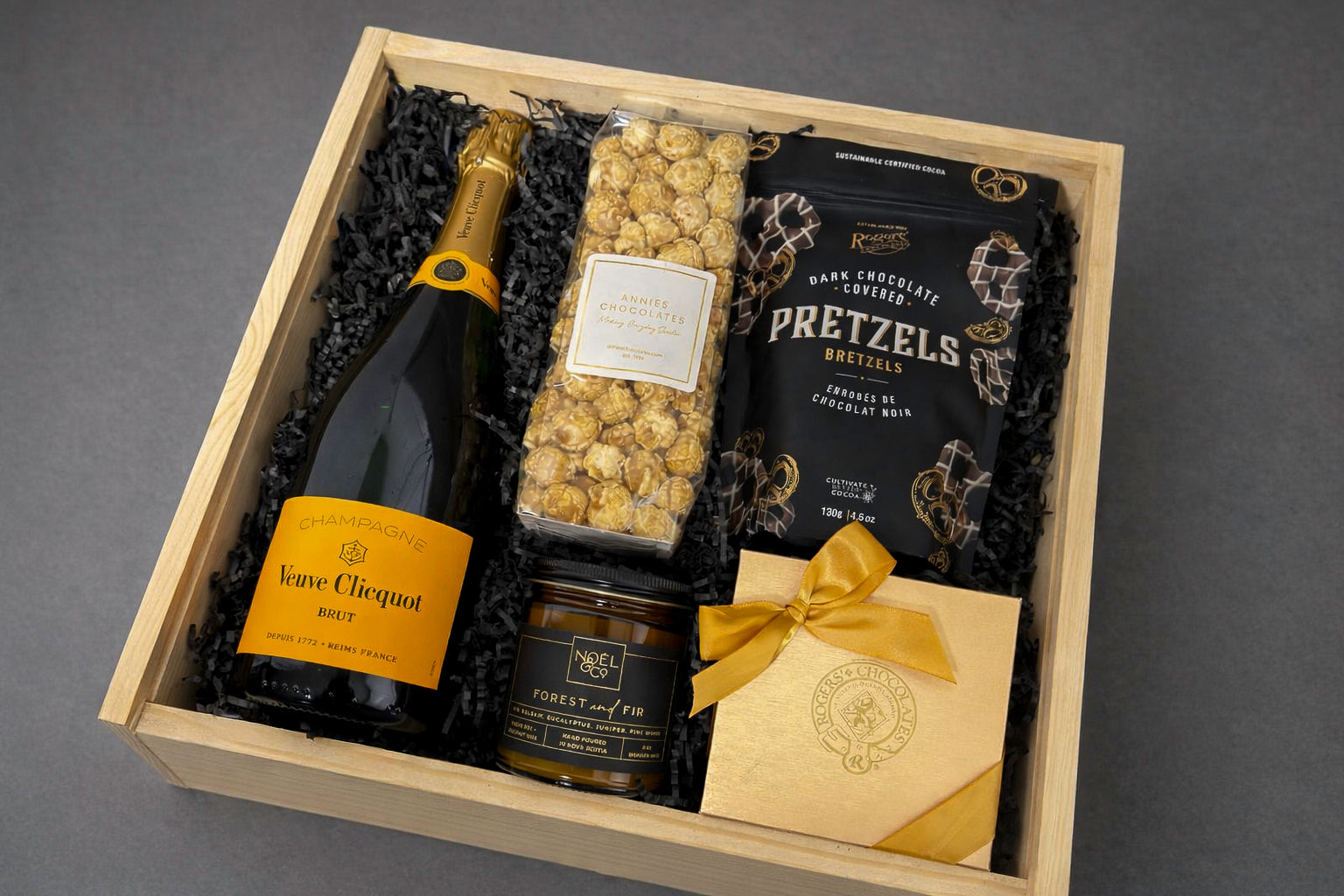 Gift basket with champagne, pretzels, popcorn, and on a grey background