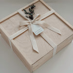 The West Village gift box from Muse Baskets and Co. shown closed, a Signature Luxe wood box tied with a cream cotton twill ribbon and dried eucalyptus, finished with a Muse Baskets and Co. gift tag reading Curated Artisan Gifting. A polished realtor closing gift, possession day gift, and corporate gift available for Vancouver, Lower Mainland, and Canada-wide delivery.