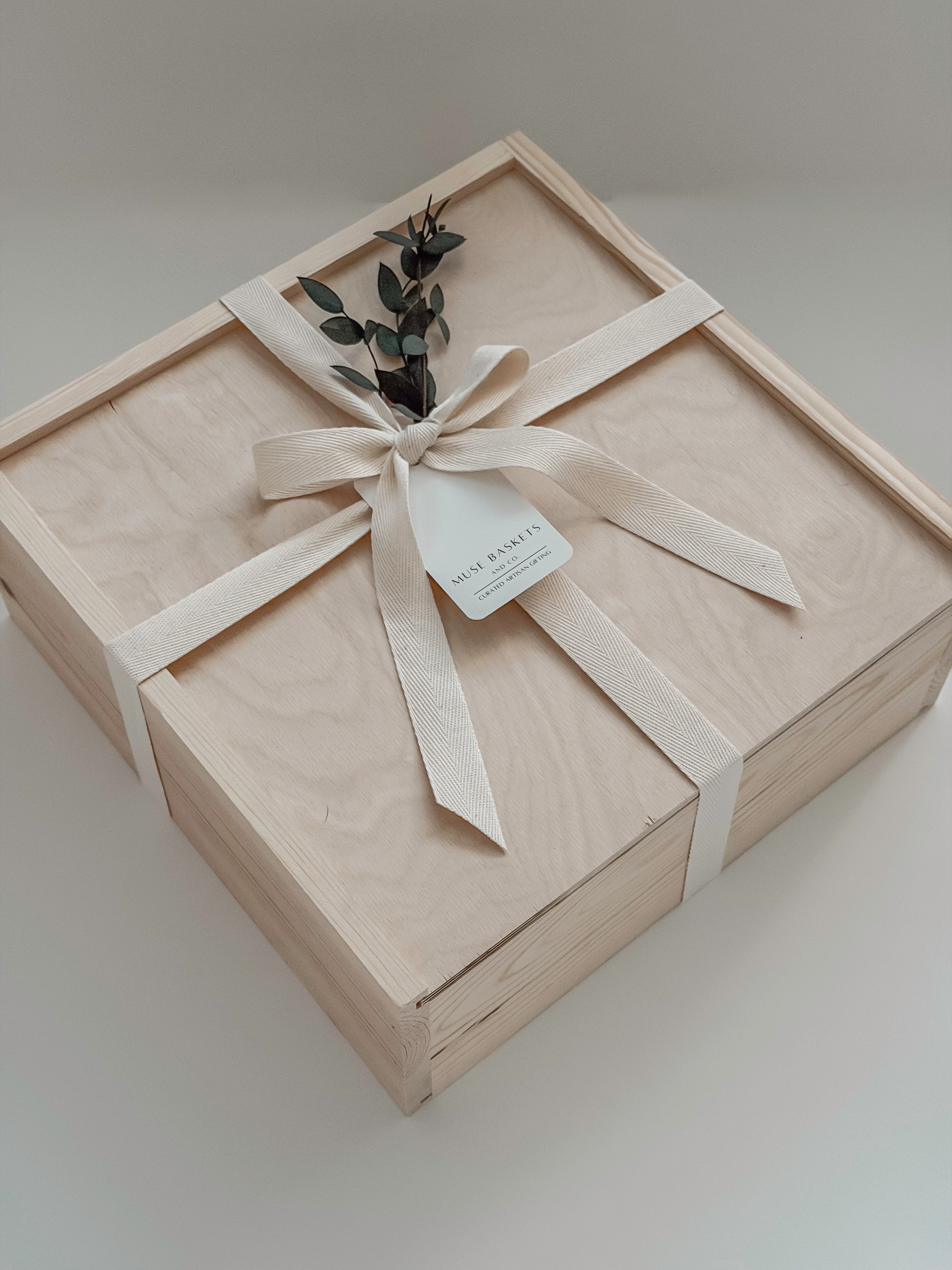 The West Village gift box from Muse Baskets and Co. shown closed, a Signature Luxe wood box tied with a cream cotton twill ribbon and dried eucalyptus, finished with a Muse Baskets and Co. gift tag reading Curated Artisan Gifting. A polished realtor closing gift, possession day gift, and corporate gift available for Vancouver, Lower Mainland, and Canada-wide delivery.