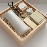 The West Village luxury gift box by Muse Baskets and Co. shown at an angle, holding a speckled white Fable carafe on its side, a Vancouver Candle Co. Silentium candle, a Laura Slack chocolate bar in gold Chiyogami wrapping, an Agha Studio Nordic Spa savon in a So Luxury bamboo dish, and a Reverie heart bath bomb with dried eucalyptus in a Signature Luxe wood box. A realtor closing gift and possession day gift for a new home.